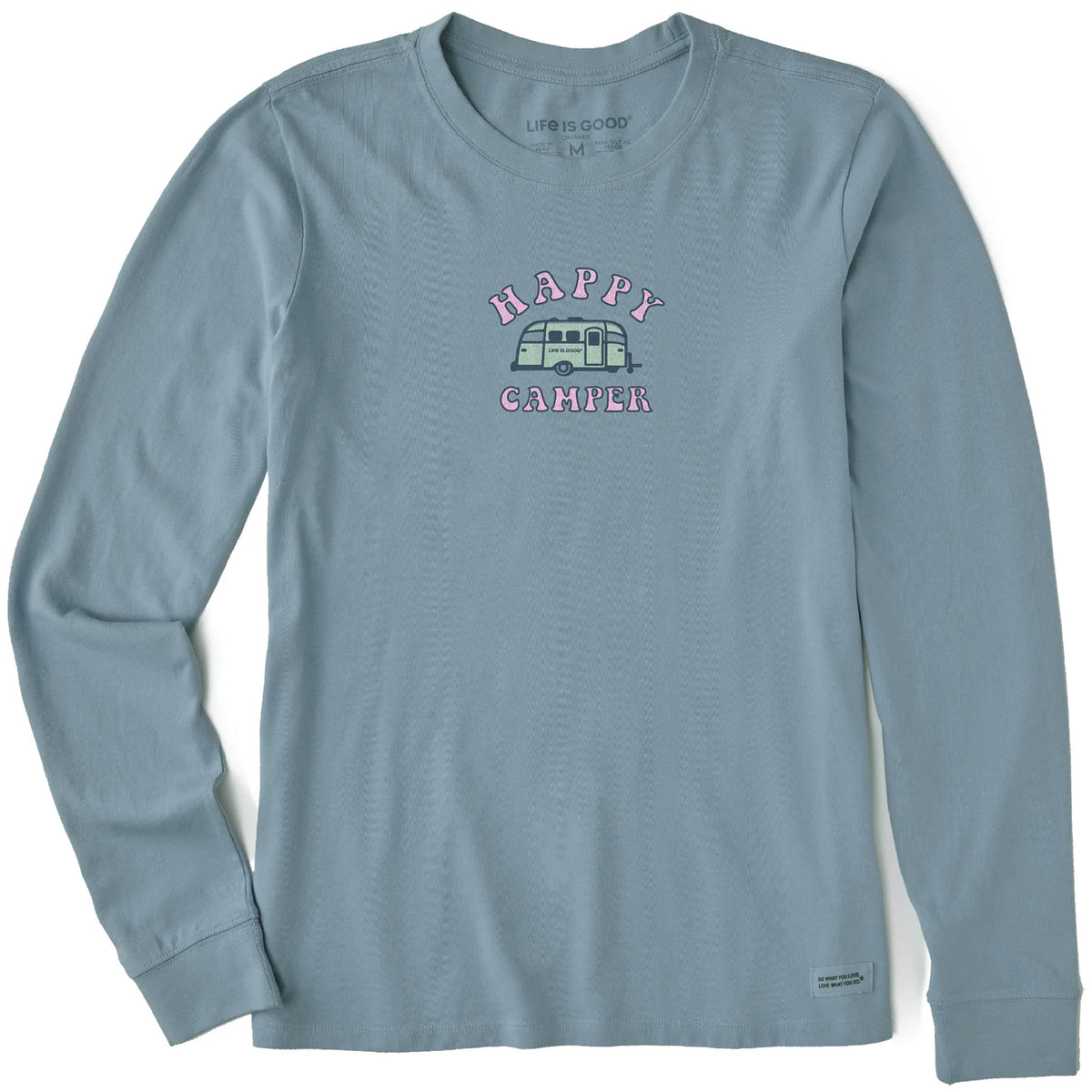 Introducing the Airstream Happy Camper Women’s Long Sleeve by Life is Good®—a light blue long sleeve shirt featuring bold “HAPPY CAMPER” text and a graphic of a green camper van, inspired by the Airstream Happy Camper spirit, centered on the chest. Perfect for anyone who loves embracing the good life outdoors!.