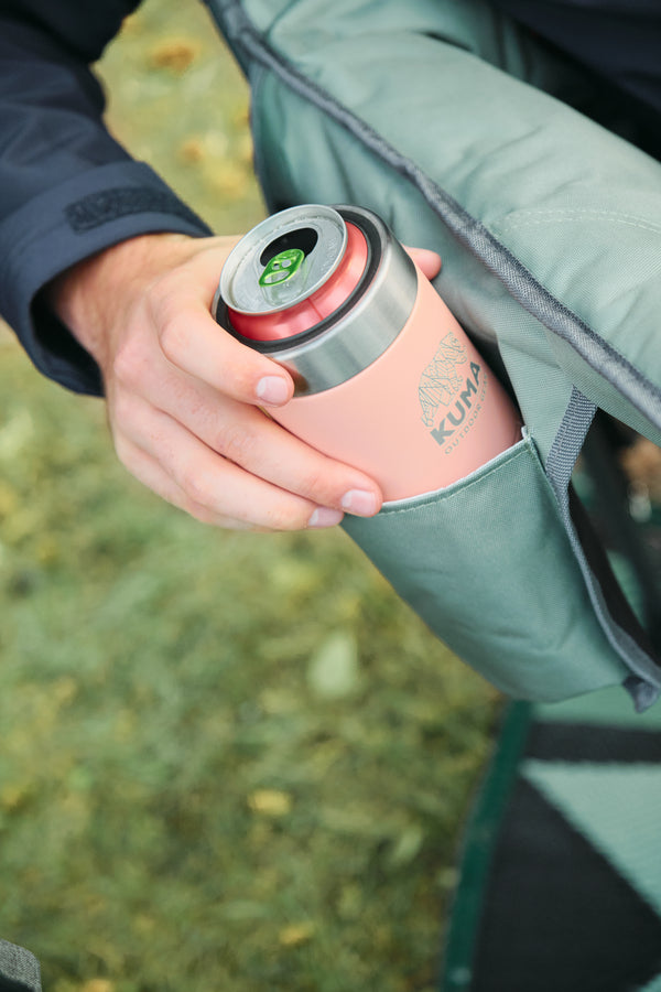 A close-up of a person holding a pink Kuvings insulated tumbler with a silver lid, tucked into a green camping chair pocket outdoors.