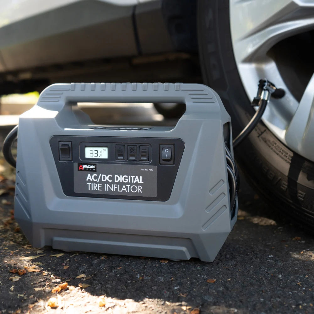 While inflating a car tire, the AC/DC Digital Tire Inflator in gray displays a reading of 33.1 PSI and sits on the ground next to the wheel, featuring an automatic shut-off function.