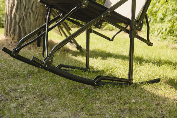 Close-up of a black metal rocking chair frame on a grassy lawn near a tree trunk in an outdoor setting.