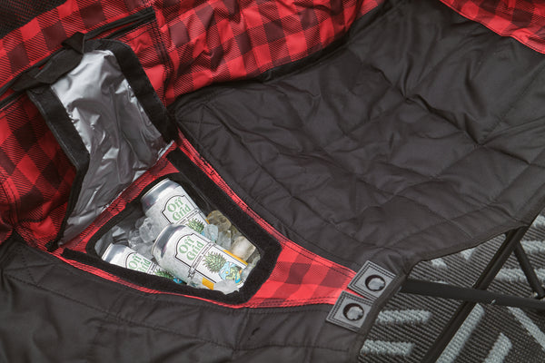 Close-up of a black quilted camping chair with a red and black buffalo plaid interior lining and a zippered storage pocket containing canned drinks.