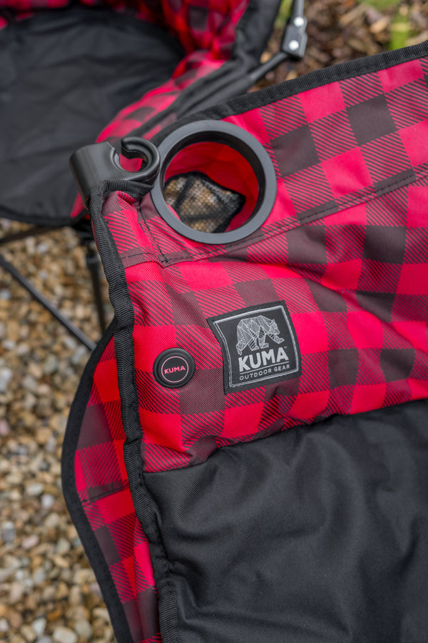Close-up of a red and black buffalo plaid camping chair fabric with a circular black cup holder and a visible Kuma brand patch.