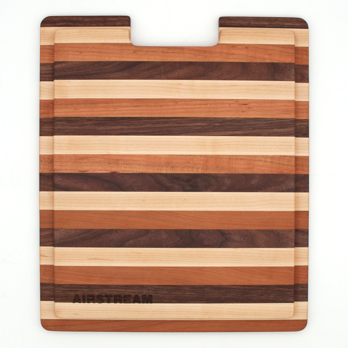 Presenting the Airstream Custom Sink Cutting Board for Interstate 24GT/GTX: a rectangular wooden board featuring alternating light and dark horizontal stripes, a convenient cutout at the top center, and “AIRSTREAM” engraved in the bottom left corner—an elegant custom accessory crafted to fit perfectly in your space.