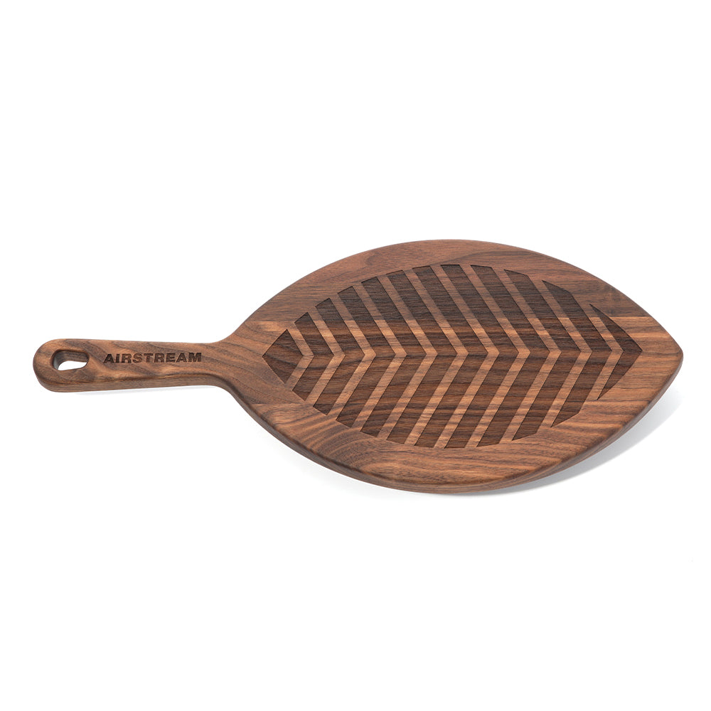 Introducing the Frank Lloyd Wright x Airstream Charcuterie Board—a leaf-shaped serving board crafted from walnut, featuring a striking engraved chevron pattern. The handle includes a hanging hole and is engraved with “AIRSTREAM,” offering an elegant tribute to Airstream and Frank Lloyd Wright design.