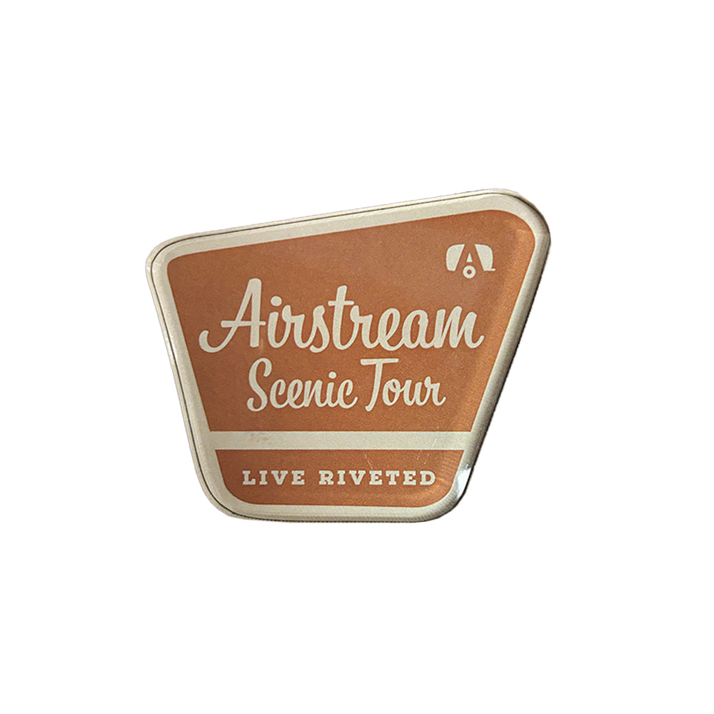 The Airstream Scenic Tour Acrylic Magnet features “Airstream Scenic Tour” in white script and “Live Riveted” below on a bold reddish background, along with a small white logo in the top right corner—making this badge-shaped acrylic magnet the perfect keepsake for Airstream fans.
