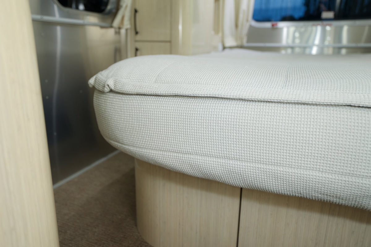 Close-up of a light-colored, textured cushion on a wooden base inside a modern, clean camper or RV interior.