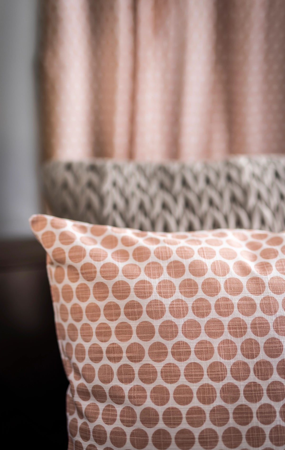 A close-up of a pillow with a peach and white geometric pattern, placed in front of Airstream Printed Custom Curtains for Pan America Travel Trailers, featuring a chevron and dot design in coordinating tones.