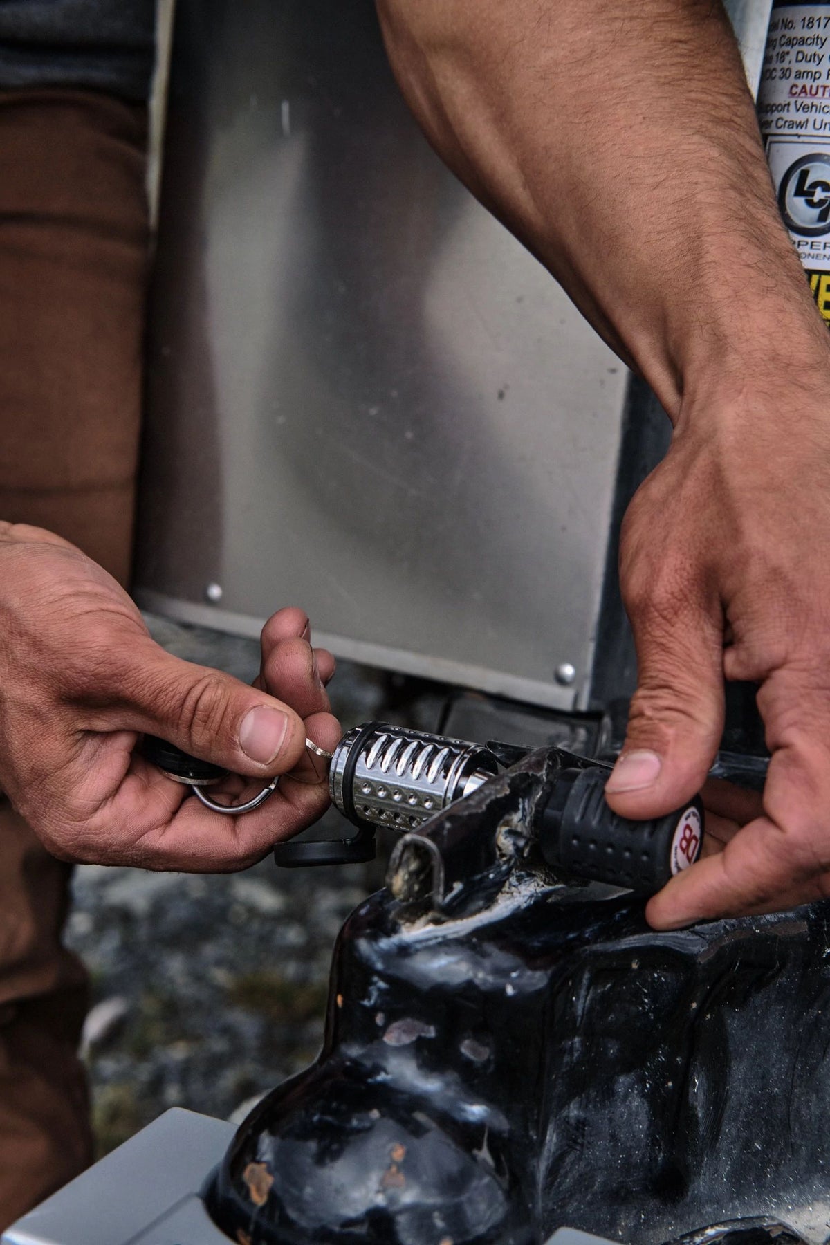 Close-up of a person’s hands unlocking or securing a combination padlock on a black metal object, with keys held in one hand and an outdoor background visible—a scene illustrating Airstream security, possibly featuring the use of the Airstream Anti-Theft Hitch and Trailer Lock Kit to protect your travel trailer lock.