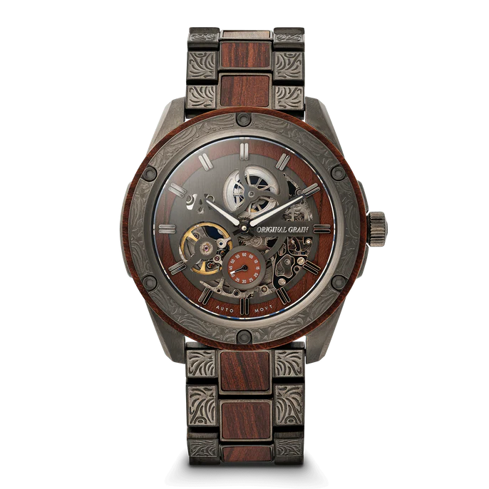 A luxury skeleton wristwatch with a dark wood and gunmetal steel link bracelet, featuring a detailed open-heart dial with visible gears and a small orange sub-dial. The brand name 'OAKRIVL GRAND' is printed on the dial.
