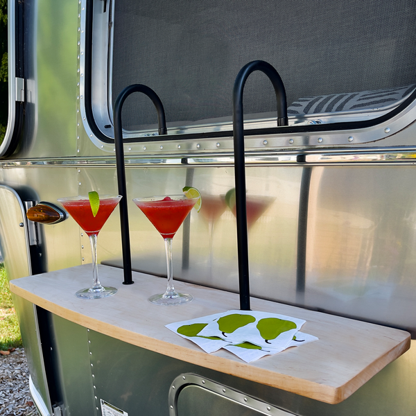 Two cocktail glasses on a wooden table with a metallic vehicle in the background