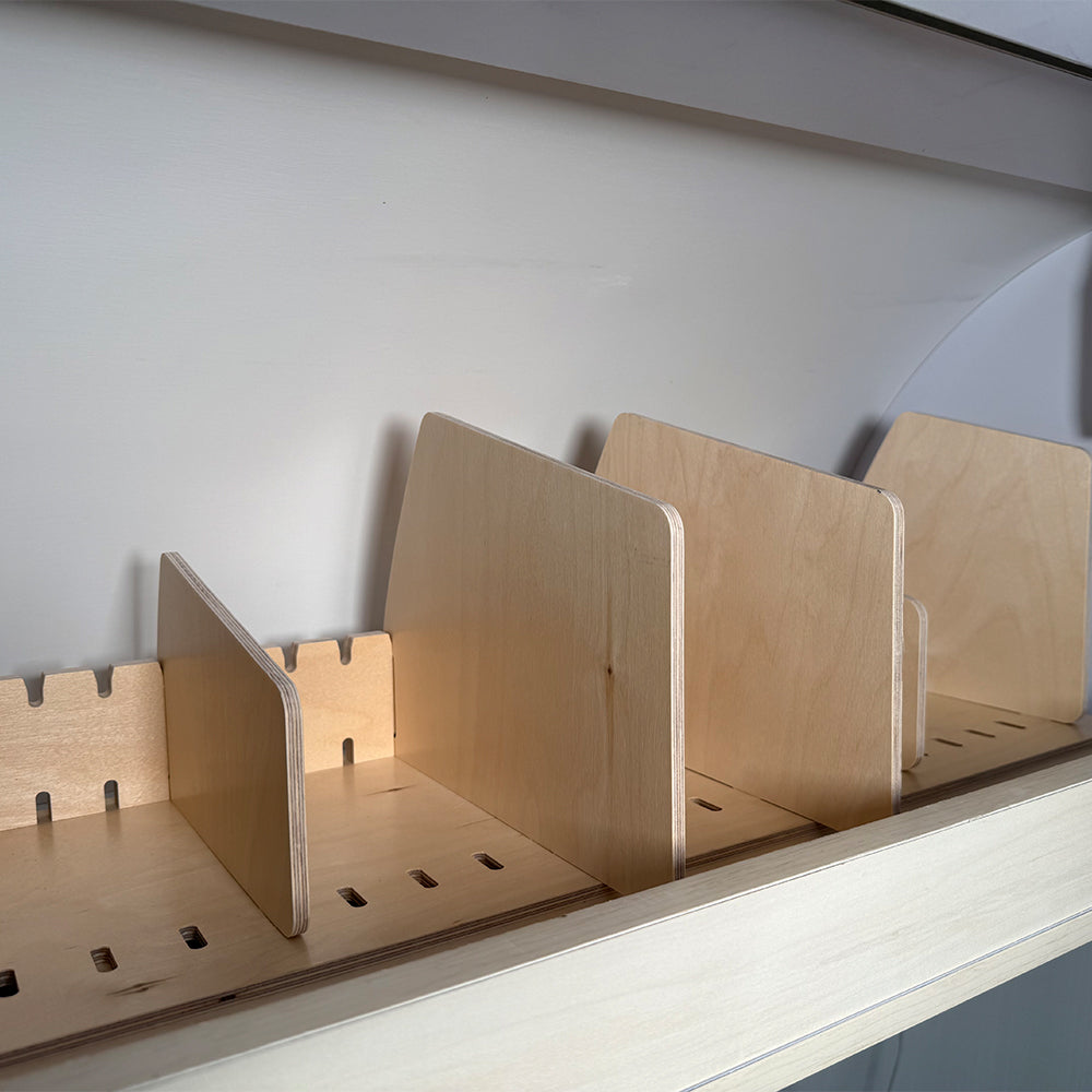 Four wooden dividers stand upright in the light wood Airstream Touring Coach Roof Locker Organization by Airworthy Equipment Company, with each slot providing efficient overhead storage against a white wall. This minimalist organizer is designed to keep papers or folders neatly arranged, making it an ideal solution for Airstream roof locker organization.