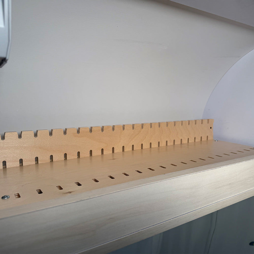 Introducing the Airstream Roof Locker Organization by Airworthy Equipment Company: a wooden shelf with evenly spaced vertical slots on the back panel, designed for adjustable shelving or organization against a white wall—ideal as an overhead storage organizer in a modular locker system.