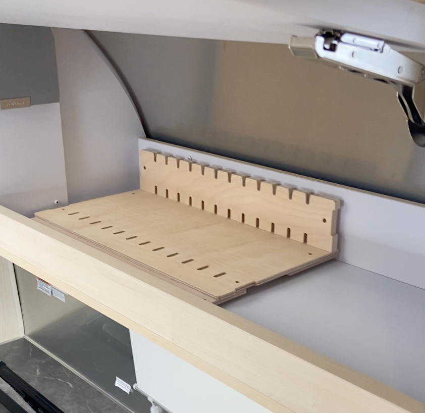 A wooden storage rack with evenly spaced slots is mounted inside a light-colored cabinet, likely designed to organize flat items like trays or cutting boards. The cabinet door is partially open at the top right.