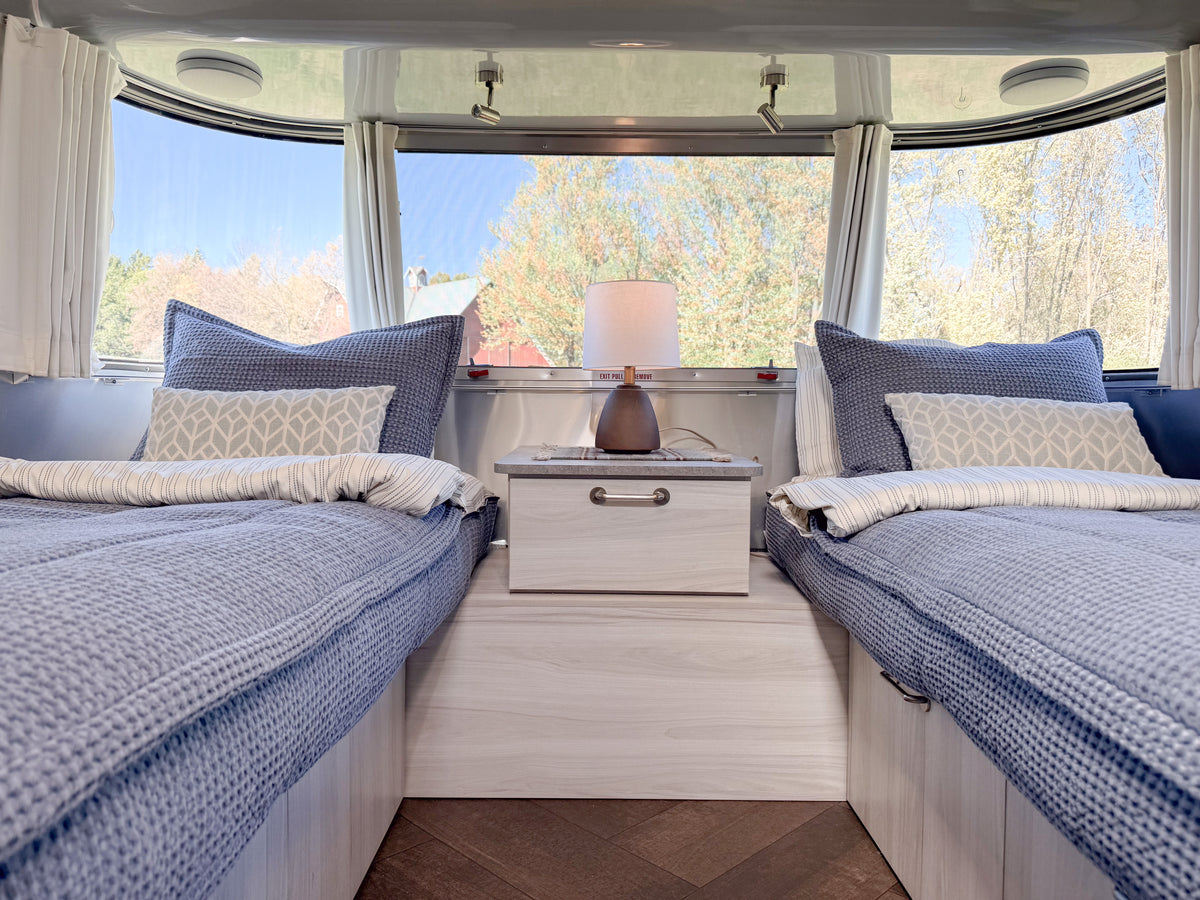 Two twin beds outfitted with Airstream Custom Fit Dual Comfort Beddy’s for Stetson + 6666 Travel Trailers, featuring textured bedding and pillows on either side of a central nightstand with a Dual Comfort ZipBase system.