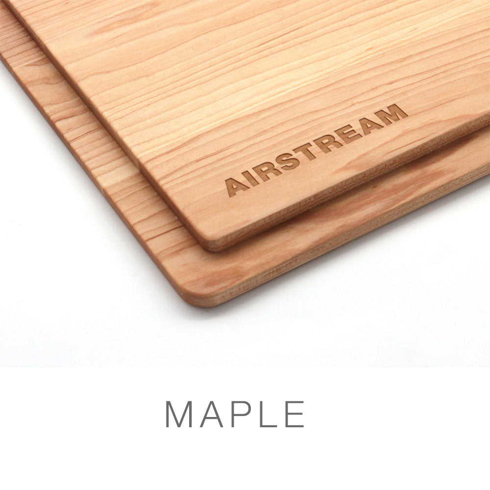 Two rectangular Airstream Custom Sink Cutting Boards for Pottery Barn Travel Trailers, crafted from maple wood, are stacked one atop the other, with “AIRSTREAM” engraved on the top board. Designed for both beauty and utility, these cutting boards make ideal custom additions to your sink setup. The word MAPLE appears beneath the boards.