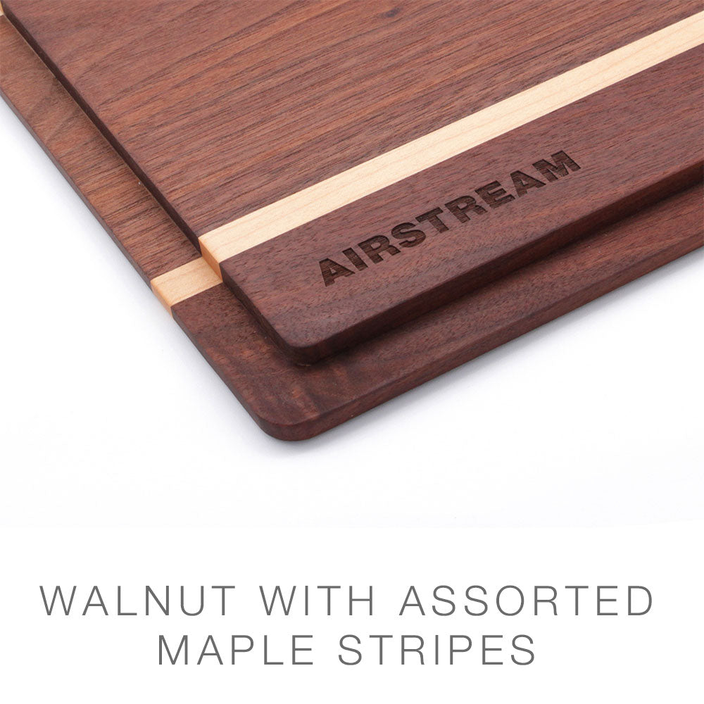 Two walnut Airstream Custom Sink Cutting Boards for Basecamp with light maple stripes; the top board is engraved with “AIRSTREAM.” These cutting boards are ideal Airstream Basecamp accessories, serving as stylish and practical additions to your travel kitchen. Text below reads: WALNUT WITH ASSORTED MAPLE STRIPES.