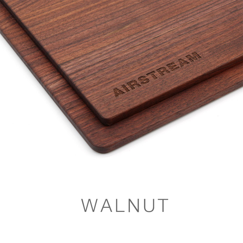 Two overlapping rectangular walnut wood boards, including an Airstream Custom Sink Cutting Board for Pottery Barn Travel Trailers engraved with “AIRSTREAM.” The walnut features a rich, dark grain. Below, the word “WALNUT” appears in uppercase letters on a white background.