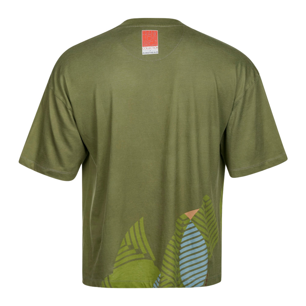 The Frank Lloyd Wright x Airstream Oversized T-Shirt is shown in olive green from the back, featuring a small red logo tag at the upper back and a leaf pattern in green, blue, and yellow near the lower right hem. This oversized T-shirt draws inspiration from architectural graphic styles for a unique and contemporary look.