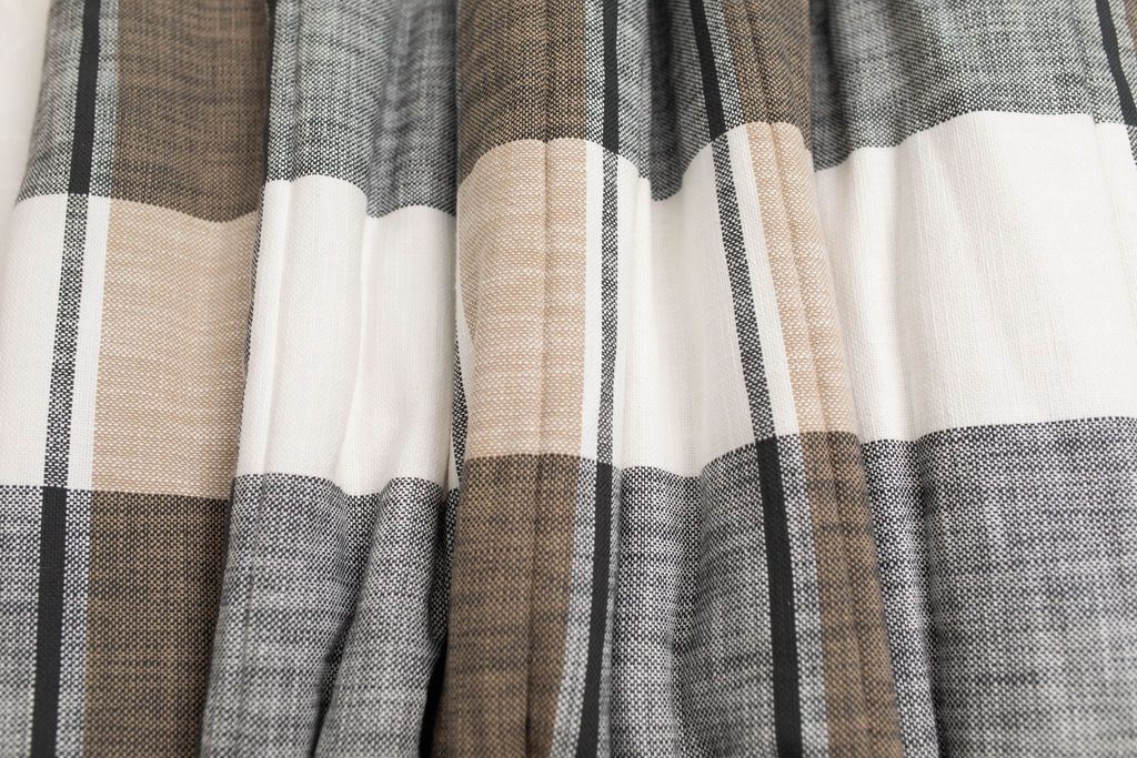 Close-up of the Erin Luxe Blanket by Beddy’s, featuring a plaid pattern in shades of gray, beige, and white with vertical and horizontal stripes and gentle folds in the fabric—perfect for adding a cozy touch to any space.