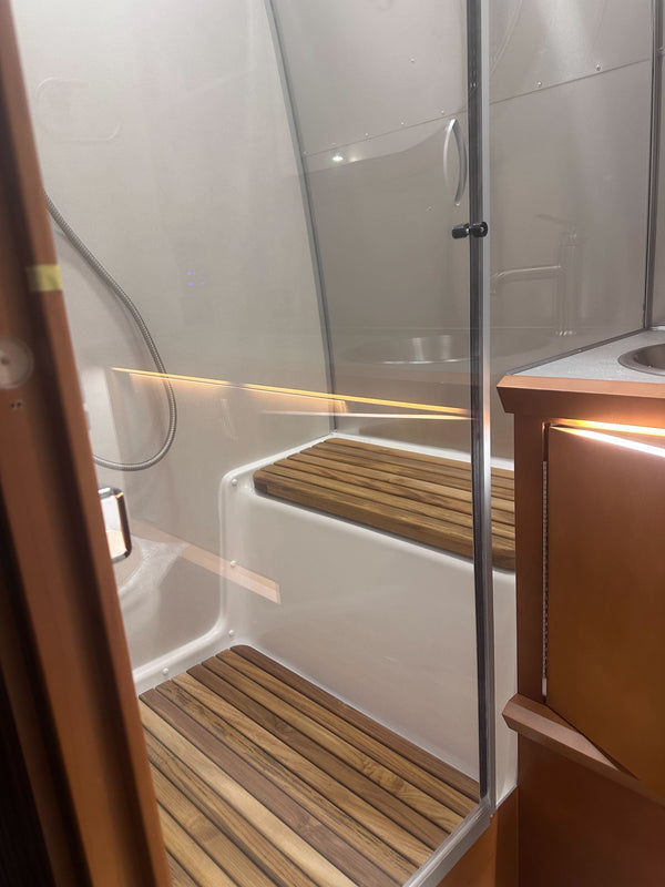 Small bathroom with shower area, wooden bench, and cabinets.