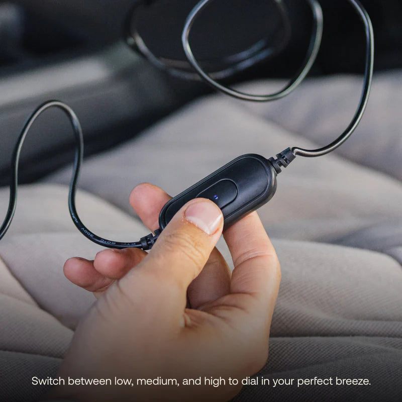 A hand holding a USB Powered Camping Fan by Luno with a button, connected by wires. Perfect for car camping or van life, this USB-C powered fan lets you switch between low, medium, and high to dial in your perfect breeze. Text at the bottom reads: Switch between low, medium, and high to dial in your perfect breeze.