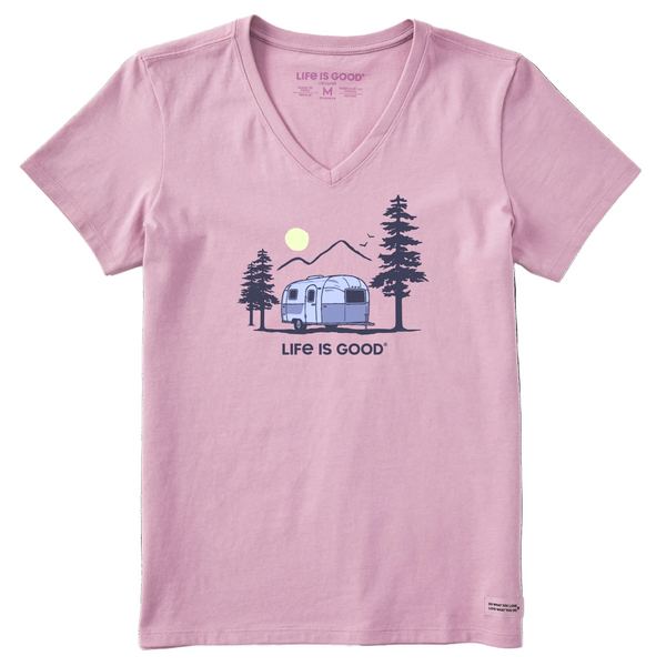 The Airstream Vintage Camp Crusher V-Neck T-Shirt by Life is Good® features a light purple color and showcases an illustration of a classic camper trailer nestled between pine trees, with mountains and a sun in the background. Below the image, “LIFE IS GOOD” is printed, making this vintage camp tee an ideal pick for outdoor enthusiasts or fans of the iconic Crusher collection from Life is Good®.