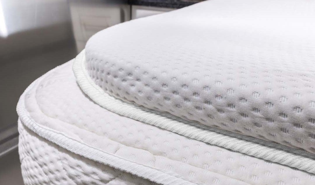 Close-up of the Airstream Memory Foam Topper for Safari Travel Trailers, featuring a white, textured surface with plush quilting and thick edging, detailed stitching, and an elegant fabric pattern—perfect as a custom-cut mattress topper for your Airstream Safari Travel Trailer.