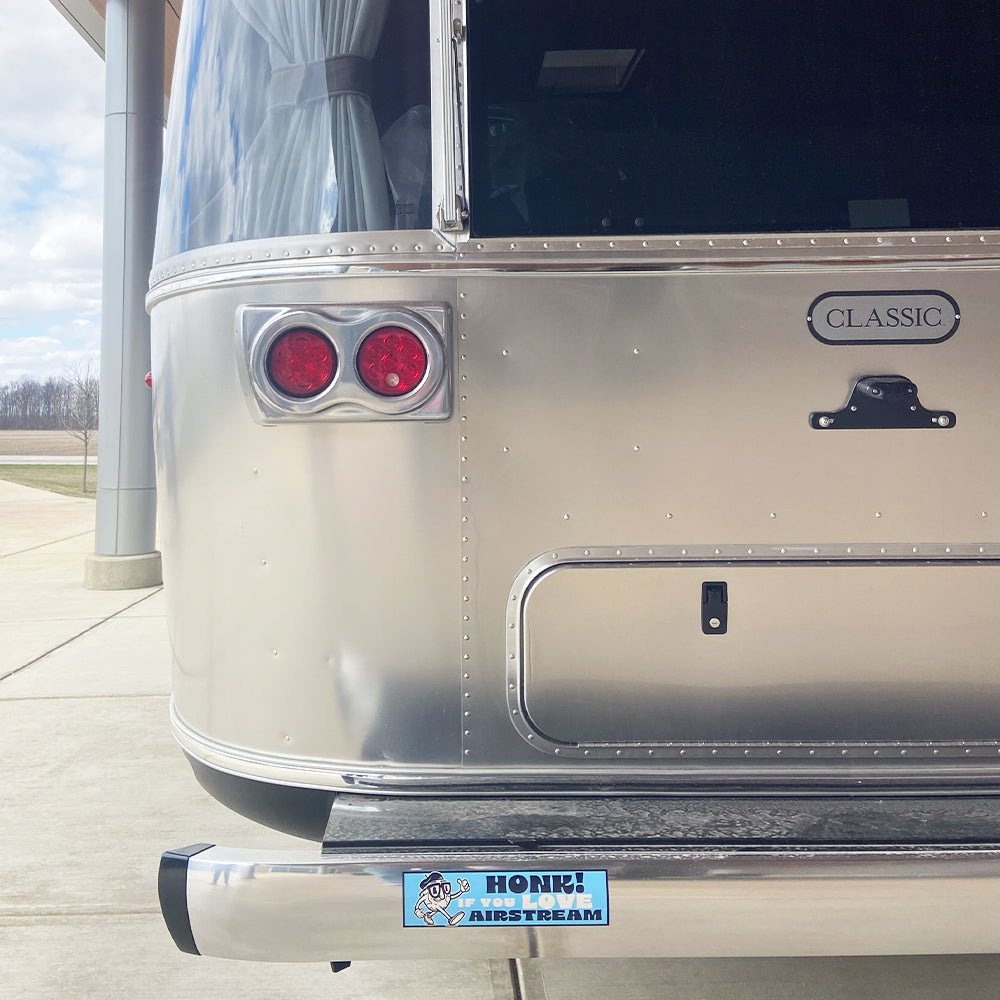Rear view of a silver Airstream trailer with a “Honk If You Love Airstream” bumper sticker featuring a cartoon dog honking a horn. The word “Classic” appears on a badge above the bumper.