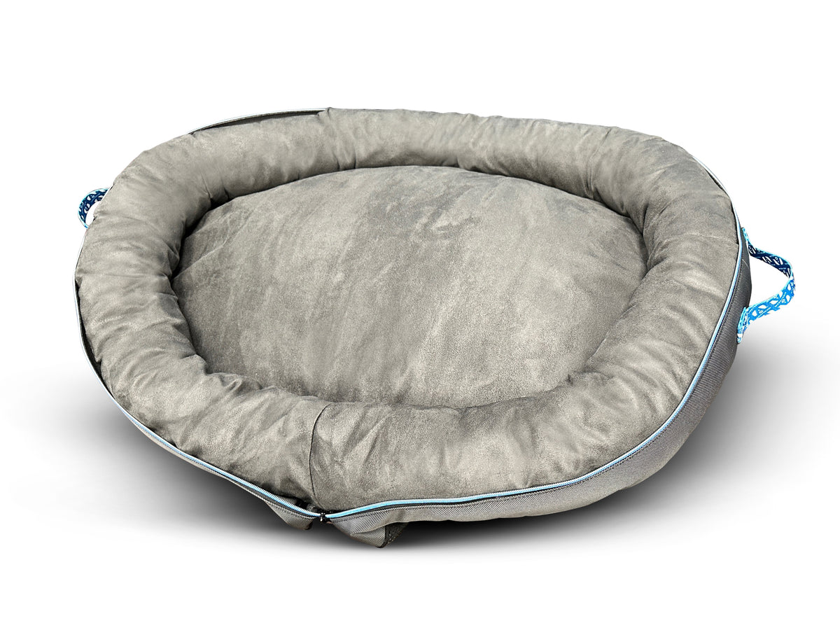The Airstream Travel Pet Bed is a round, plush gray portable pet bed featuring raised edges, blue braided carrying handles, and light blue piping, shown here on a white background.