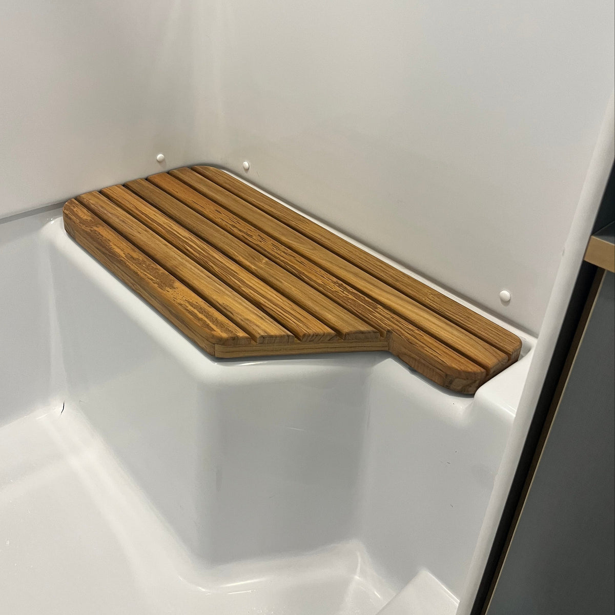 A close-up view of the Airstream Teak Shower Mat for World Traveler Travel Trailers placed in the corner of a white shower or bathroom area. The mat features a rectangular design with rounded edges, combining style and functionality as one of the elegant custom Airstream accessories.