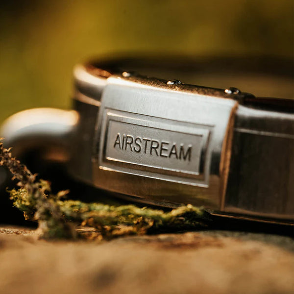 Close-up of a metallic belt buckle with 'Airstream' branding on a blurred natural background