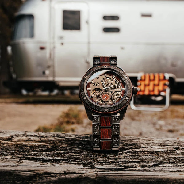 Steampunk-style watch on a wooden surface with a vintage trailer in the background