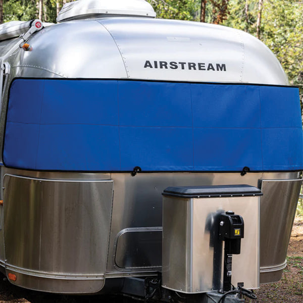 A silver Airstream travel trailer featuring a blue Airstream Travel Trailer Padded Solar Window Guard Protector is parked outdoors, surrounded by trees. #color_Blue