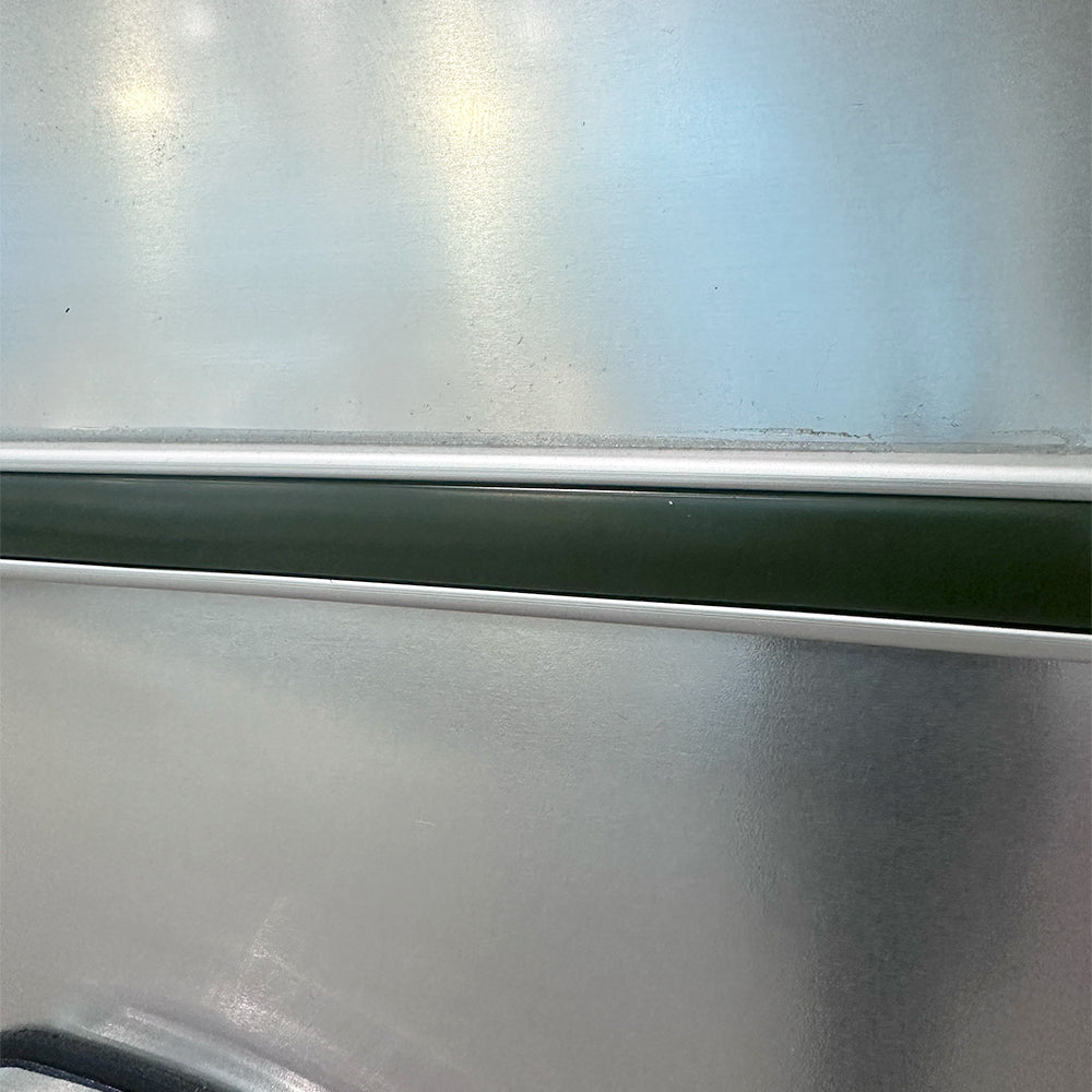 A close-up of a metallic surface with a glossy finish, featuring a horizontal dark green stripe bordered by thin white lines near the middle—showcasing the Airstream Premium Replacement Belt Trim for Travel Trailers, an accessory inspired by classic aluminum Airstream exteriors.