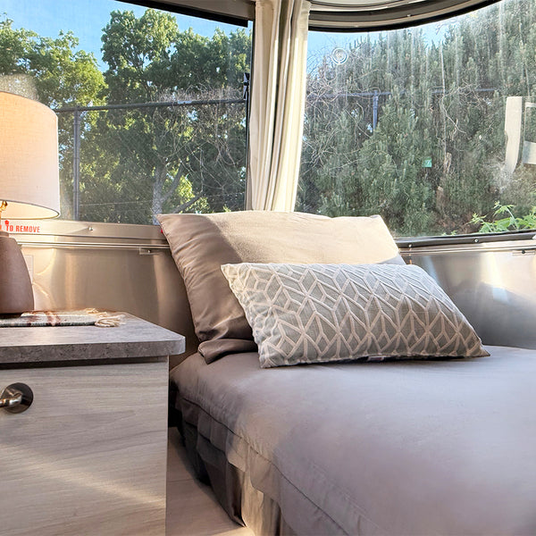 Bedroom with a bed and nightstand next to large windows with a view of trees.