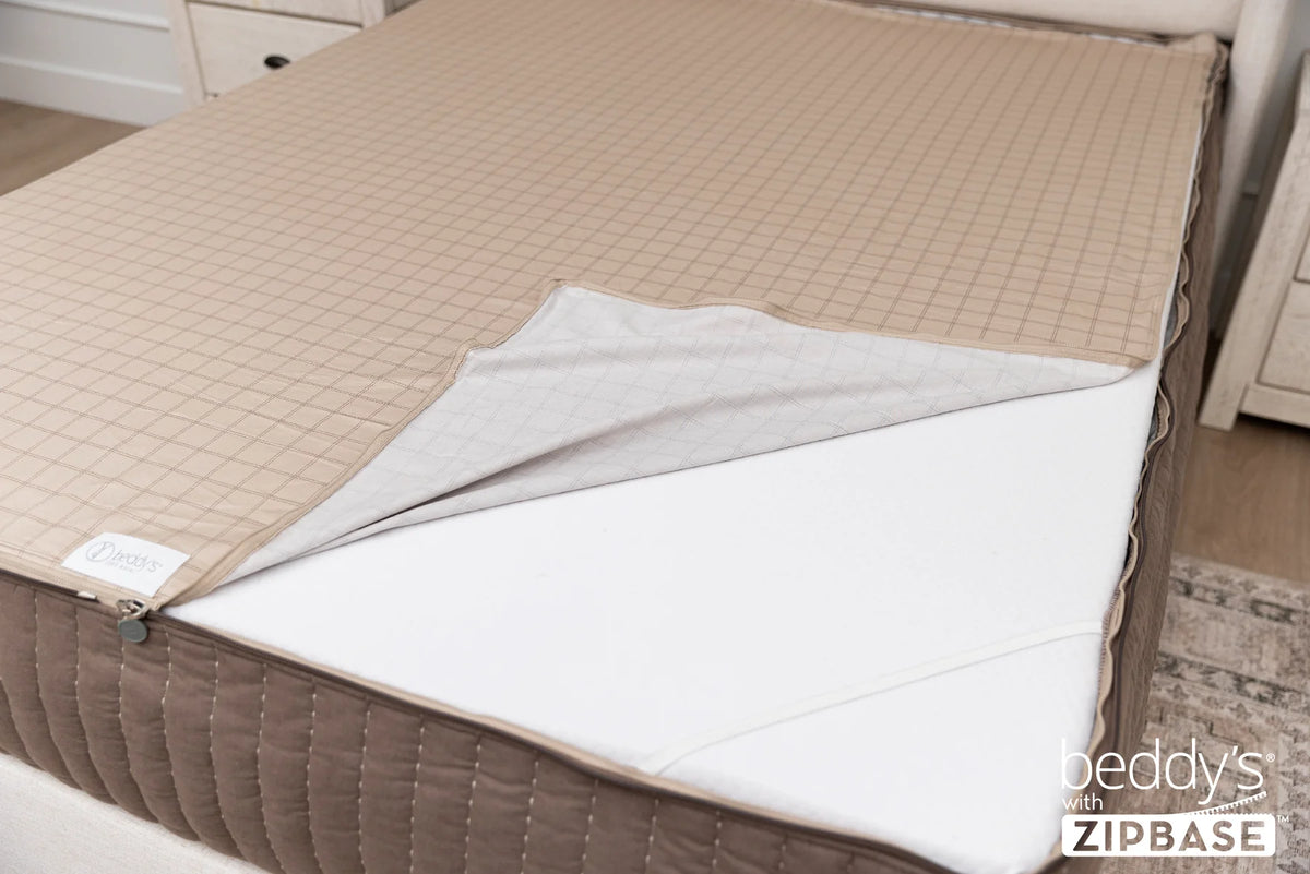 A close-up of a bed featuring the Airstream RV Fit Beddy’s for Flying Cloud Travel Trailers shows a beige zippered mattress cover partially opened to reveal a white mattress beneath. Set in a modern bedroom, this convenient all-in-one bedding offers effortless style and comfort. “Beddys with ZIPBASE” appears in the bottom right corner.
