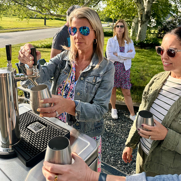People at an outdoor event with a bar setup and people in the background.