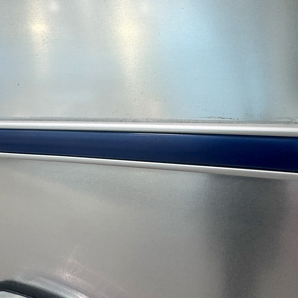A close-up of the Airstream Premium Replacement Belt Trim for Travel Trailers shows a metallic surface with a horizontal blue and white stripe running across it. The trim features a smooth, reflective aluminum texture with soft reflections created by the lighting.