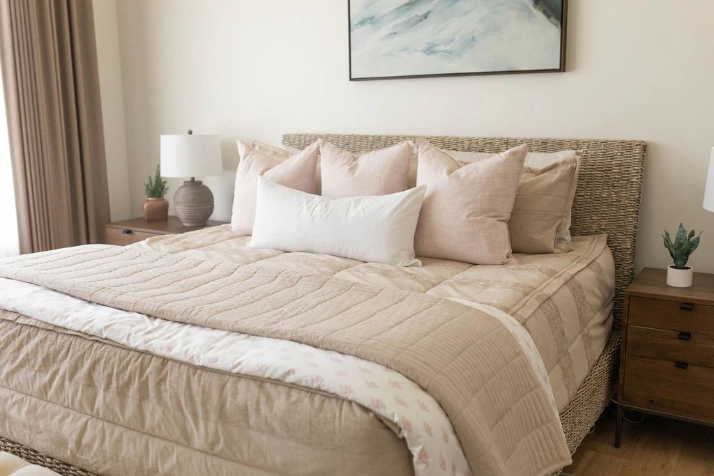 Featuring the Airstream RV Fit Beddy’s for Excella Travel Trailers, this serene bedroom setup showcases zippered bedding in elegant beige for effortless style and easy convenience—perfectly designed for your RV or Airstream oasis. The plush bed includes five pillows and a cozy beige comforter, complemented by two wooden nightstands with lamps, a small plant accent, and a framed abstract painting above the headboard. Soft neutral tones create an inviting, tranquil atmosphere ideal for relaxation on the road.