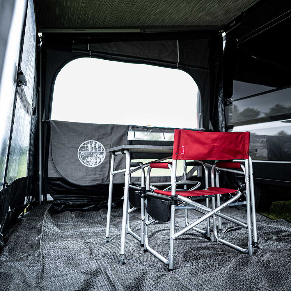 Two red folding camp chairs with metal frames are set up inside a Buddy Awning Enclosure for the Airstream Rangeline, which features premium Isacryl material; a window and door are visible in the background.
