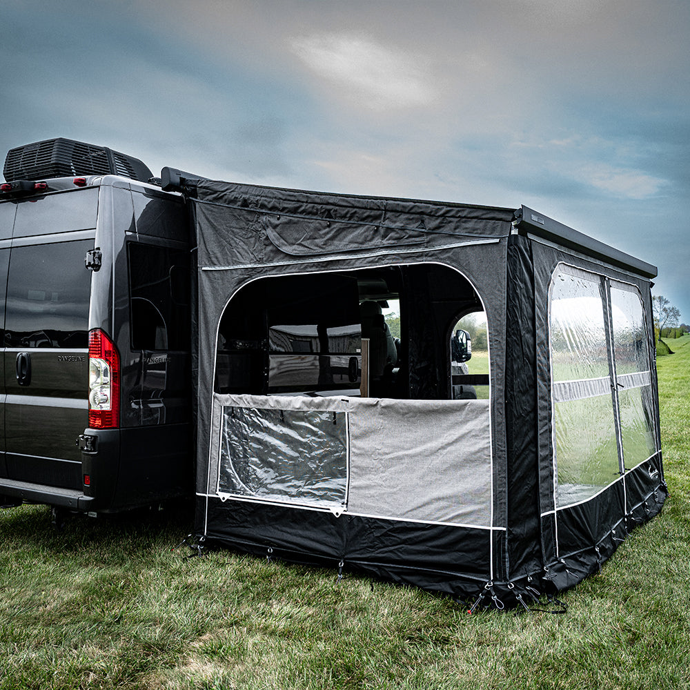 A black van with an attached Buddy Awning Enclosure for Airstream Rangeline creates a tent-like space featuring clear and mesh panoramic windows, set up on grassy ground under a cloudy sky.