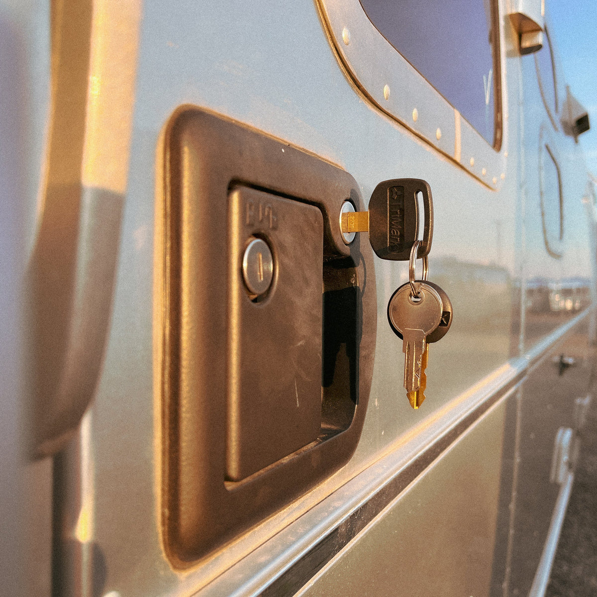 A close-up of an Airstream Pre-Cut Key for Deadbolt Main Door inserted into the lock of a metallic RV or trailer door, with reflections of the surroundings visible on the shiny surface.