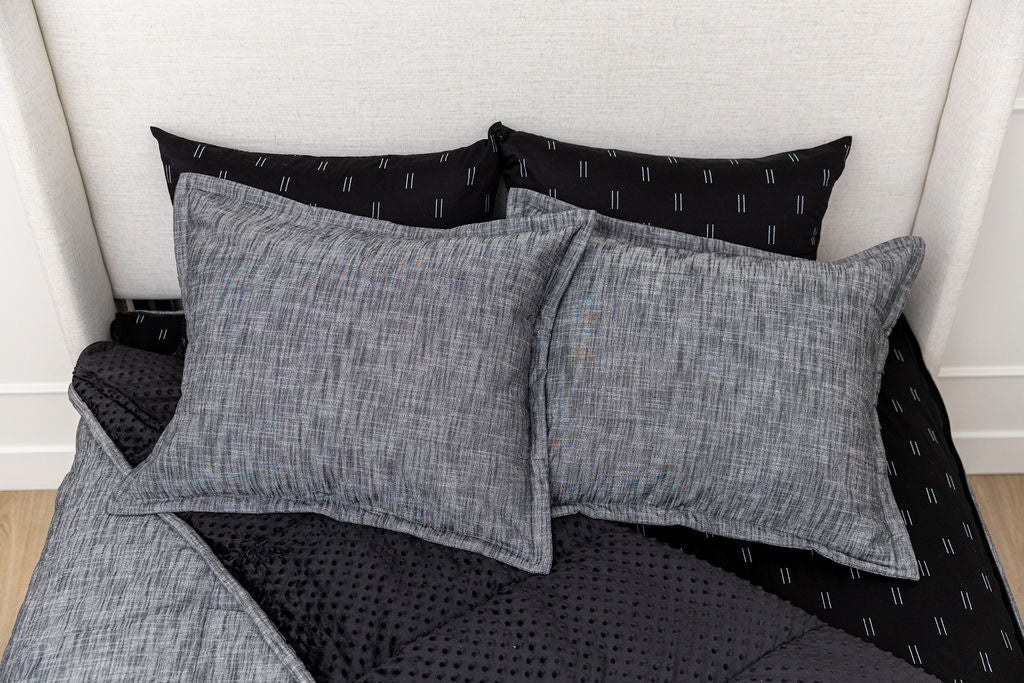 Two gray textured pillows rest on top of two black pillows with white lines, all arranged on a black dotted comforter and light bed frame—an ideal setup for Airstream RV Fit Beddy’s for Excella Travel Trailers.