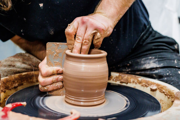 Person working on a clay pot on a pottery wheel