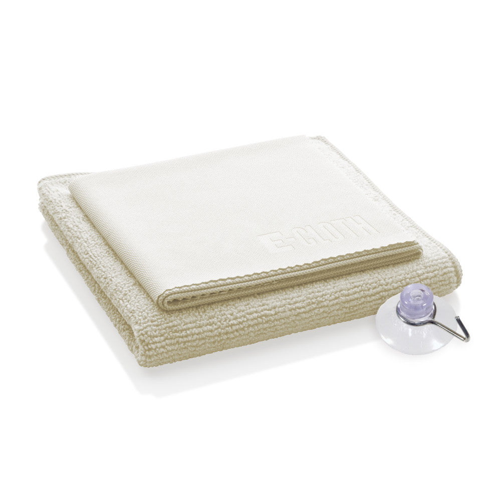 A folded beige microfiber cloth, embossed with “E-CLOTH,” sits next to a clear suction cup featuring a small metal hook, representing the chemical-free Shower Cleaning Kit by E-Cloth.
