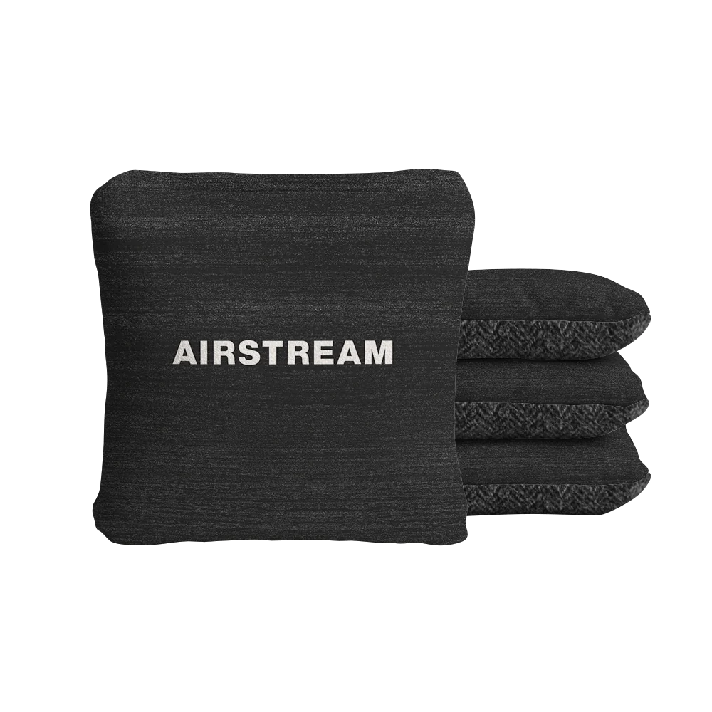 Four black square Airstream ACA Cornhole Bags, one positioned at the front displaying the word “AIRSTREAM” in bold white letters and three arranged side by side behind it, all set against a plain white background—showcasing a modern, clean style reminiscent of custom cornhole bags.