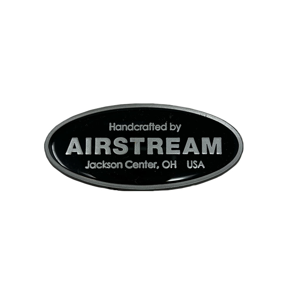 A 3″ oval black medallion featuring the authentic Airstream logo and “Handcrafted by Airstream, Jackson Center, OH USA” in silver text—official Part #386068-01. Ideal as a replacement emblem or for those seeking genuine Airstream parts. Shown on a plain white background.