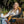 A woman sits in a black and tan camping chair outdoors, smiling while holding a white insulated tumbler. Another person in the foreground holds a matching tumbler.