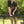 A man wearing a black Puma t-shirt and shorts is assembling a black metal folding table outdoors on a grassy lawn with trees in the background.