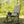 A black and gray folding camping rocking chair with a built-in cup holder, set outdoors on a grassy lawn with a background of green trees.